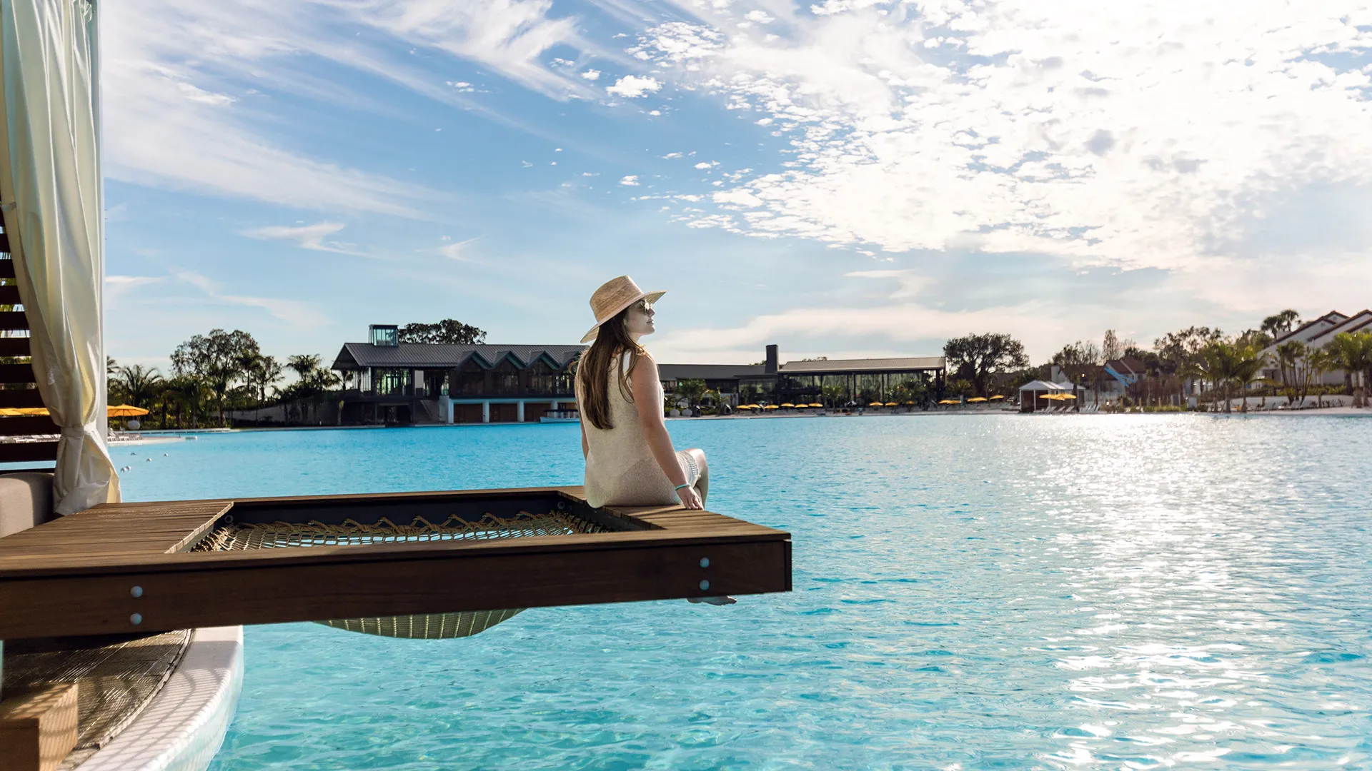 Private Overwater Cabana on Evermore Bay An image of a woman relaxing by the netting of the overwater hammock in a private cabana on Evermore Bay at Evermore Orlando Resort.